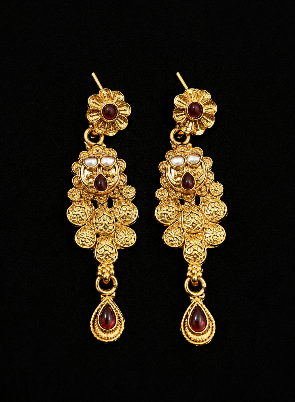 Pair of gold earrings with floral designs and red gemstones on a black background