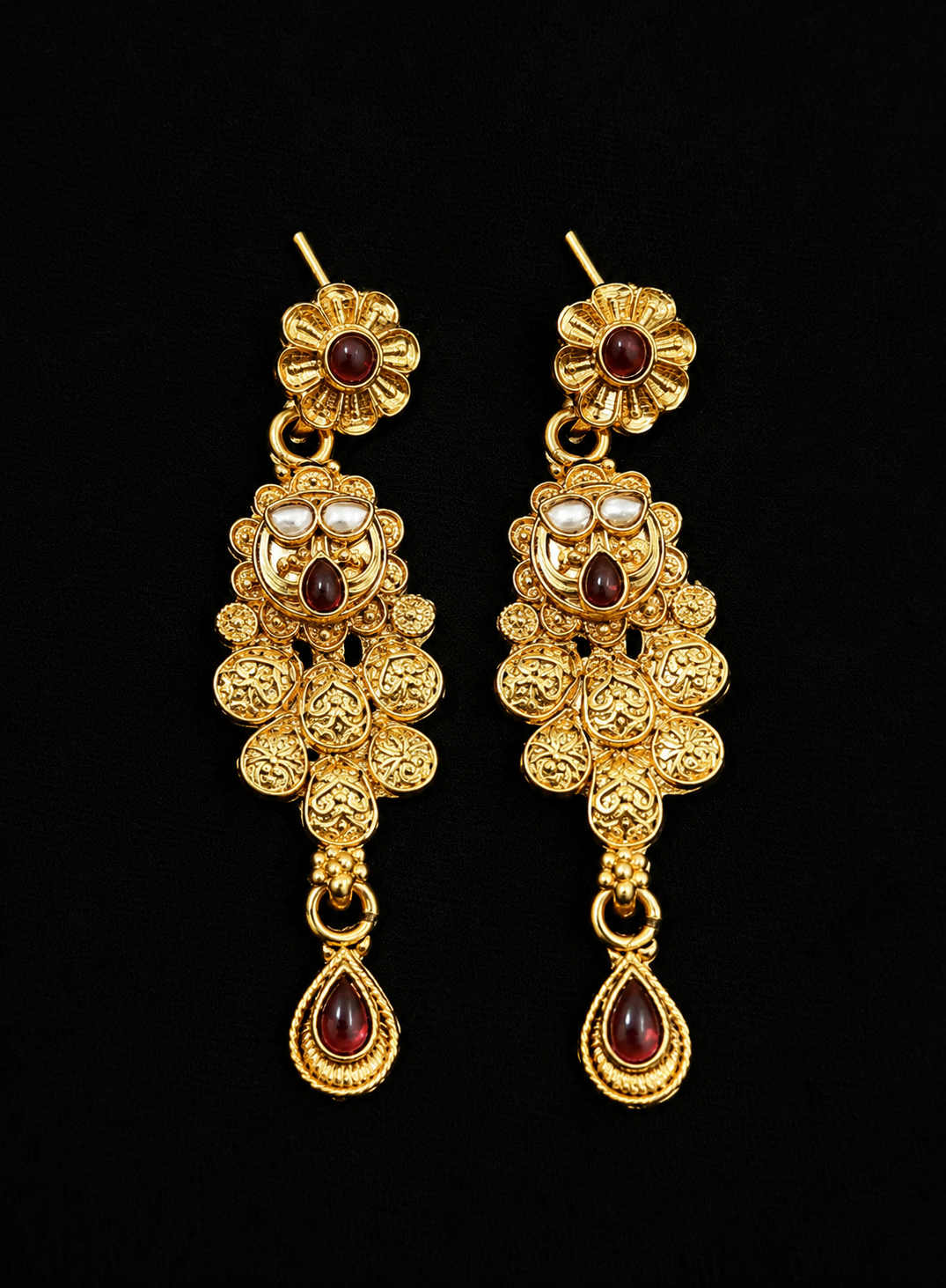 Pair of gold earrings with floral designs and red gemstones on a black background